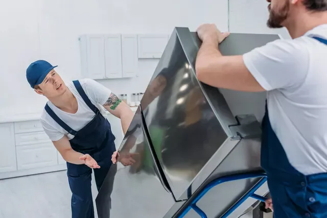 שני מובילים מרימים מקרר בעזרת עגלת הובלה