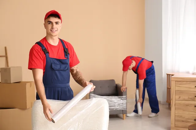 מוביל מחזיק גליל ניילון נצמד ליד כורסה עטופה ומוביל שני עובד מאחוריו