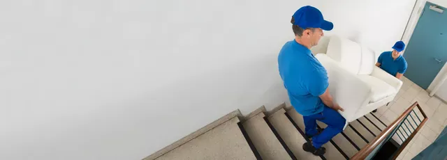 שני מובילים בחולצות כחולות נושאים ספה לבנה במורד חדר מדרגות, מבט מלמעלה