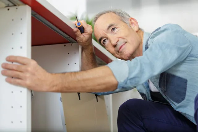 גבר מבוגר מהדק במברג רהיט לבן בזמן הרכבת ארון